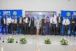 A group of individuals, dressed formally, stand on a stage holding awards. Two "SAPS" banners are in the background. The mood is celebratory.
