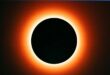 A glowing orange halo encircles a dark, centered circle, resembling a solar eclipse, set against a dim background, evoking a sense of mystery.