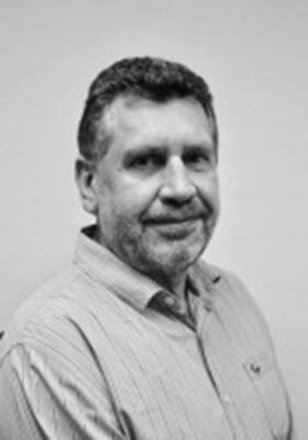 Portrait of a man with short hair and a beard, wearing a striped shirt, smiling slightly, in black and white, conveying a calm and approachable demeanor.