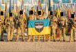 Seven armed soldiers in uniform pose for a photo while holding a flag with a skull emblem and the words "Thorne Group," surrounded by various flags.