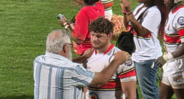 A man is being congratulated by a diverse group of people, smiling and clapping in a celebratory atmosphere.