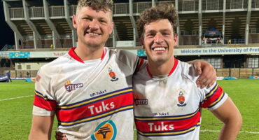 Two rugby players stand on a field at night, illuminated by stadium lights, ready for the game to begin.