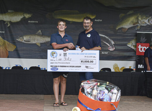 Two people smiling and shaking hands at a fishing competition. They hold an oversized check for prize money. Fish graphics are displayed in the background.