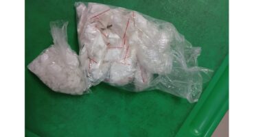 Bags of white powder and crystal-like substances on a green surface, possibly illicit drugs. The mood is tense and concerning.