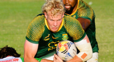 A rugby player, with the ball in hand, is in the midst of being tackled by an opposing player