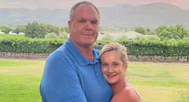 A man and woman embrace in front of a majestic mountain backdrop, conveying warmth and connection.