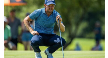 A man crouches on the green, preparing to putt during a golf game.