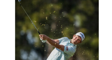 A golfer in mid-swing, striking a golf ball on a lush green fairway