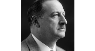 A black and white photo of a Oscar Henry Frewin wearing a suit, standing confidently with a serious expression.
