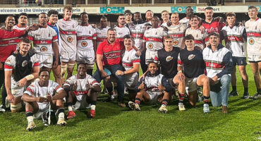 A group of men and women standing together, posing for a photo on a sunny field.