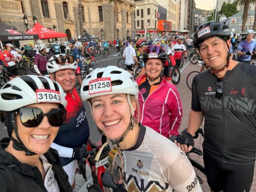 A group of people on bicycles smiling and posing together for a photo outdoors.