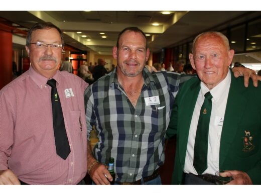 Three men in a social setting, dressed in formal and casual attire, smiling and enjoying each other's company. Name tags visible.