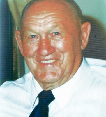 An older man wearing a white shirt and blue tie, looking confidently at the camera