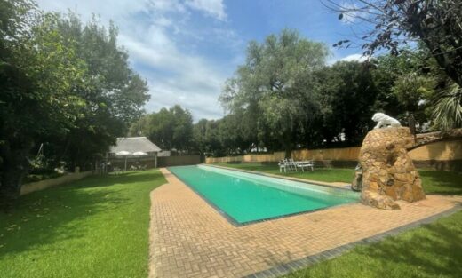 A tranquil pool in a resort, shaded by a large tree, creating a peaceful atmosphere for outdoor enjoyment.