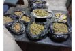 Numerous black bags filled with marijuana buds and smaller packages of various items are spread across a dark, textured table indoors.