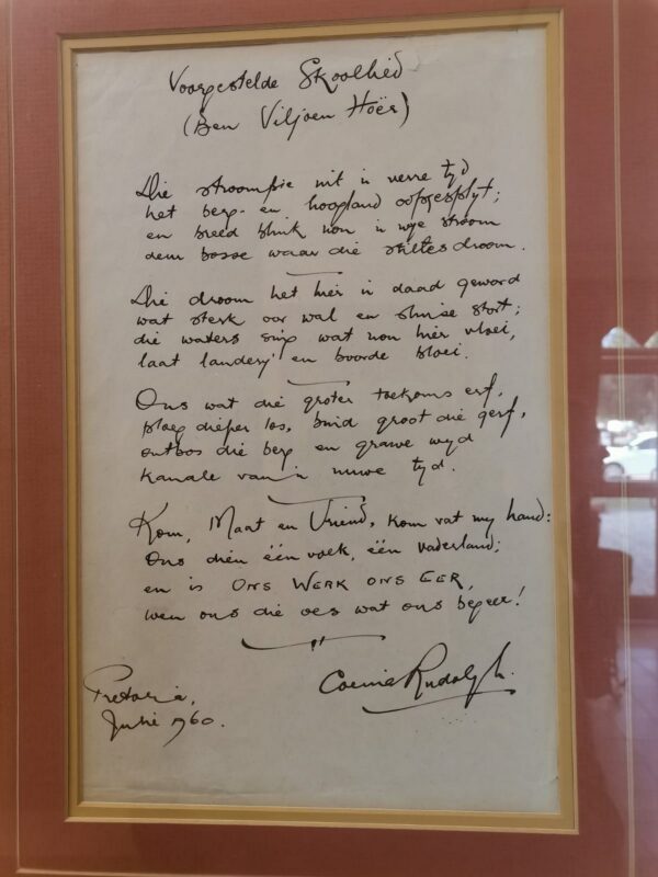 A framed handwritten poem titled "Voorgestelde Skoollied" in Afrikaans, dated June 1960, Pretoria. It conveys a patriotic tone, signed at the bottom.