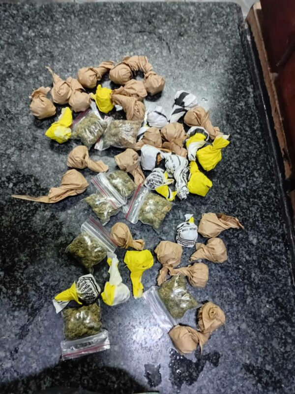 Various small packages, including colorful paper bundles and clear plastic bags with green herbs, are scattered on a dark speckled surface.