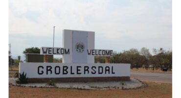 A large entrance sign reads "Welkom Welcome Groblersdal," surrounded by sparse vegetation and a cloudy sky, creating a welcoming atmosphere for visitors.