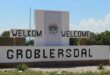 Welcome sign for Groblersdal in a rural area, featuring text in English and Afrikaans. The sky is clear and the scene is peaceful and inviting.