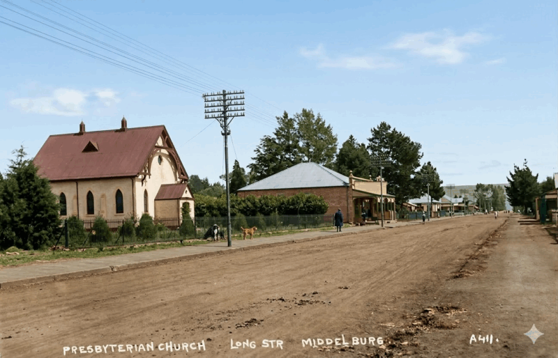 Dirt road lined with a church and houses on Long Street, Middelburg. A solitary figure walks with a dog under a clear blue sky, evoking a serene rural scene.