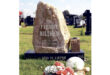 A tall, rustic gravestone with "Freddie Mileham" inscribed stands on a grassy cemetery. Flowers at the base. The tone is peaceful and solemn.