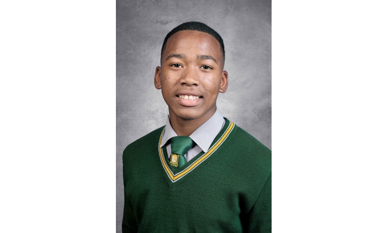 A young person smiles warmly, wearing a green sweater with yellow and gray stripes over a gray shirt and green tie. The background is a textured gray.
