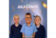 Three smiling children in school uniforms stand in front of a blue backdrop with "AKADEMIE Top 3" written above. Gold confetti decorates the image.