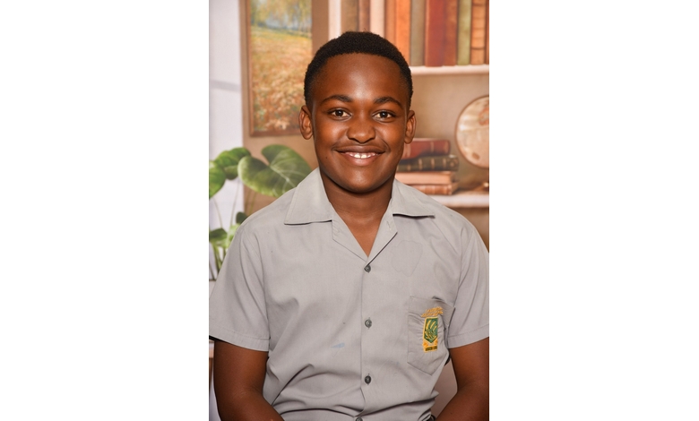A teenage boy wearing a grey school uniform with an emblem smiles warmly. In the background, there are books and a globe, creating an academic setting.