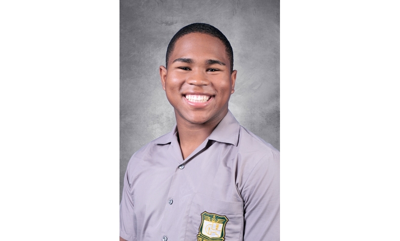 Smiling young person wearing a light gray shirt with a green and yellow embroidered emblem, set against a textured gray background conveying a joyful tone.