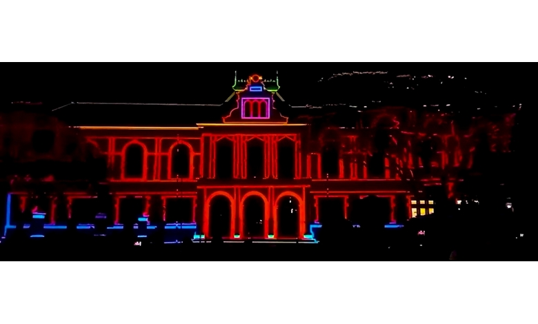 A historic building is illuminated with vibrant neon lights, displaying red, blue, and green outlines. The scene conveys a lively and festive atmosphere.