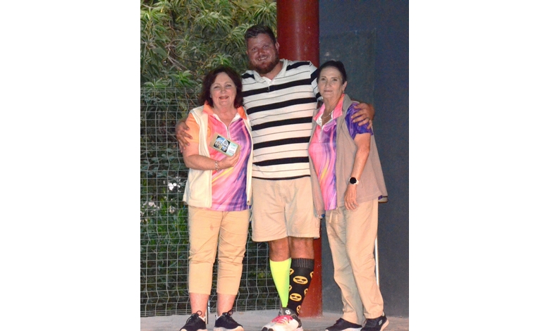A smiling man in a striped shirt stands between two women in matching purple and pink tops. They are in an outdoor setting, exuding a friendly, casual vibe.
