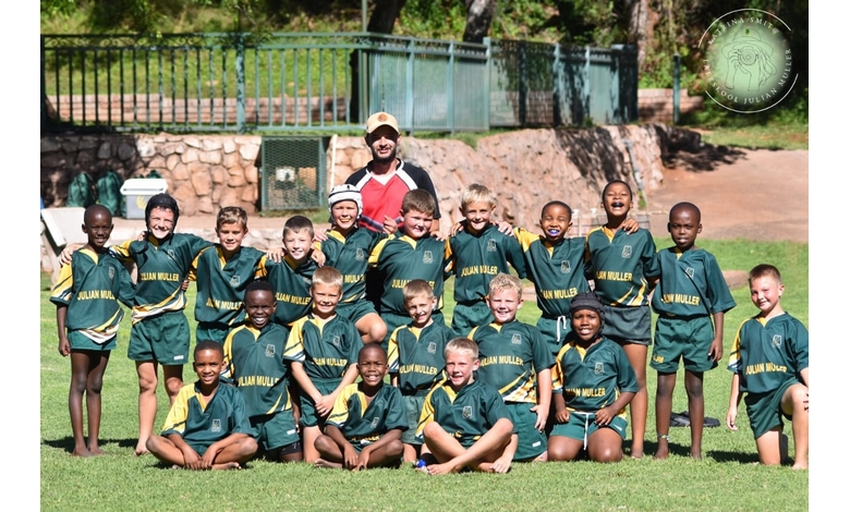 A joyful group of young boys in green and yellow sports uniforms pose together on a grassy field with their coach, expressing excitement and team spirit.