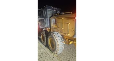 A large construction vehicle with thick tires parked on a brick surface at night. It has a yellow body, visible CAT logo, and emits a warm glow.