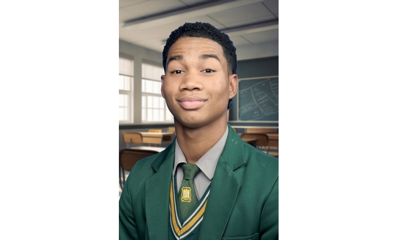 A young man in a green school uniform and tie smiles confidently in a classroom with large windows and a chalkboard. Bright, academic atmosphere.