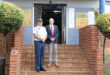 Two men stand in front of a community service center. One is in a police uniform and the other in a suit. The mood is formal and welcoming.