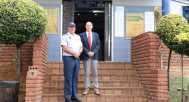 Two men stand in front of a community service center. One is in a police uniform and the other in a suit. The mood is formal and welcoming.