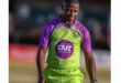 A smiling cricketer in a green and purple uniform with "Outsurance" logo walks on the field, conveying a sense of joy and accomplishment.