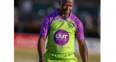 A smiling cricketer in a green and purple uniform with "Outsurance" logo walks on the field, conveying a sense of joy and accomplishment.