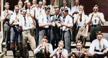 A group of young men in vintage attire gather on stairs, enjoying drinks and snacks. They wear suspenders and ties, exuding a joyful, camaraderie-filled atmosphere.