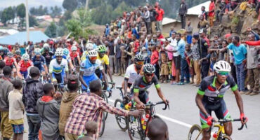 A group of cyclists in colorful jerseys race on a road lined with cheering spectators. The crowd adds vibrancy and excitement to the event.
