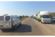 A long line of trucks and an ambulance on a clear highway under a bright sky. The vehicles are heading in the same direction, suggesting a traffic delay.
