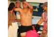 A shirtless rugby player appears injured, holding his head with a pained expression. He is surrounded by concerned onlookers and teammates in sports attire.