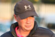 A man wearing a dark cap and puffer jacket gazes to the side. The sunlight highlights his face, conveying a contemplative mood.