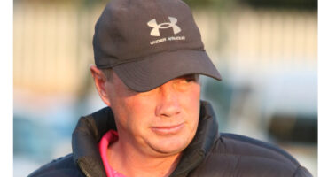 A man wearing a dark cap and puffer jacket gazes to the side. The sunlight highlights his face, conveying a contemplative mood.