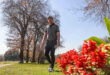 Man in golf attire walks on a sunny course, surrounded by autumn trees and vibrant red flowers, creating a serene and focused atmosphere.