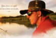 A serene lakeside scene at sunset features a person in a camo hat and sunglasses fishing. Text reads, "Gone from our sight, but never from our hearts."