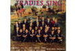 A group of boys and a few adults, dressed in school uniforms, are posed on a lawn with a garden and building in the background. The image has a nostalgic, formal tone. The text reads "Tradies Sing" and mentions the Boys' Choir of the Technical High School, Middelburg, Transvaal.