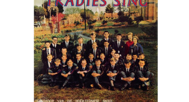 A group of boys and a few adults, dressed in school uniforms, are posed on a lawn with a garden and building in the background. The image has a nostalgic, formal tone. The text reads "Tradies Sing" and mentions the Boys' Choir of the Technical High School, Middelburg, Transvaal.