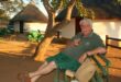 ‘n Man sit op ‘n bankie in die wildtuin.