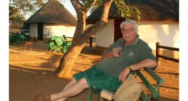 ‘n Man sit op ‘n bankie in die wildtuin.